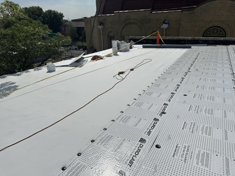 Single-ply membrane sheets being installed across a roof field